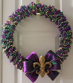 a purple, green and gold beaded wreath with a fleur de lis bow