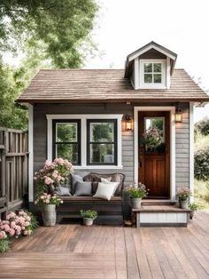 a small gray and white house with flowers on the porch