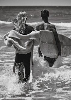 two people carrying surfboards into the ocean