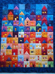 a quilted wall hanging on the side of a building with colorful houses in it