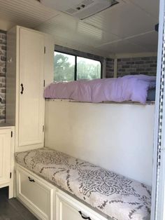 a white bunk bed sitting next to a window in a room with built in cabinets