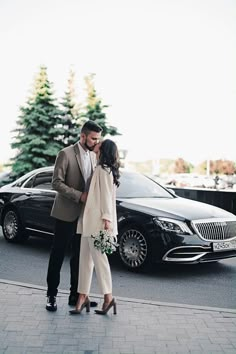 a man and woman standing next to each other in front of a car