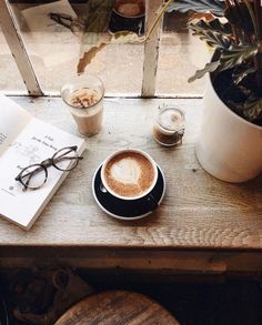 a cappuccino on a table next to a book, glasses and a potted plant