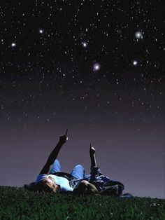 two people laying on the grass under stars in the night sky with their hands up