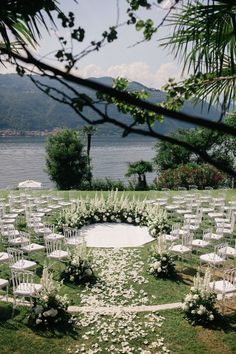 an outdoor ceremony setup with white chairs and flowers on the grass, overlooking water in the background