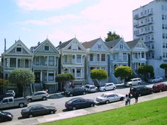 many cars parked on the street in front of row houses with tall buildings behind them