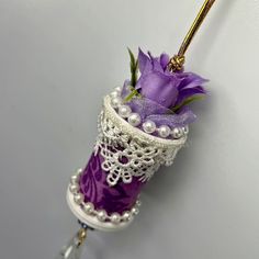 a purple flower in a white vase with pearls and lace on the top, hanging from a hook