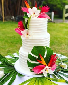 there is a white cake with flowers on the top and green palm leaves around it