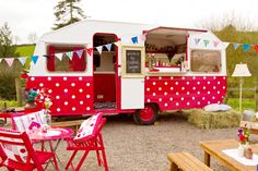 a red and white food truck is parked in the gravel with tables and chairs around it