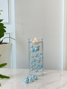 a glass vase filled with blue balls on top of a table next to a potted plant