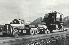 an old photo of a semi truck hauling a large load down a road in the mountains