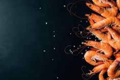 raw shrimp on a black background with salt and pepper sprinkled around the edges