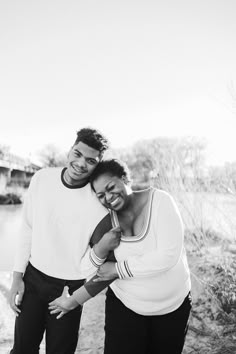 a man and woman standing next to each other in front of a body of water