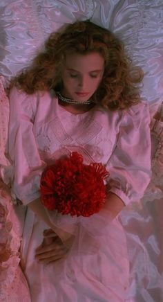 a woman laying on top of a bed holding a bouquet of red carnations