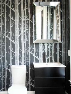 a white toilet sitting next to a black and white wallpapered bathroom with trees on it