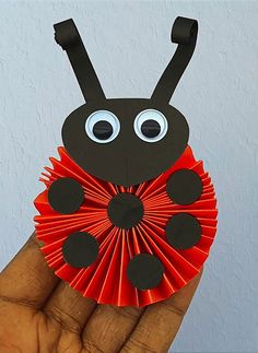 a hand holding up a red and black paper ladybug origami decoration