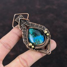 a hand holding a piece of jewelry with a blue stone in it's center