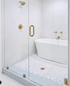 a white bathtub sitting next to a walk in shower under a bathroom mirror with gold handles