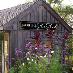 a wooden building with purple flowers in the foreground and a sign that says carib's she shed