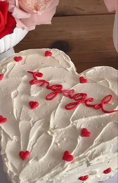 a heart shaped cake with the word love spelled in red icing on it next to pink roses