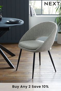 a grey chair sitting on top of a wooden floor next to a table with a plant