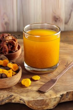 a glass of orange juice next to two bowls of dried fruit on a cutting board