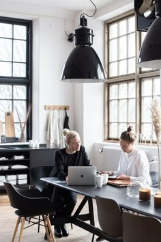 two women sitting at a table working on their laptops in an industrial style office