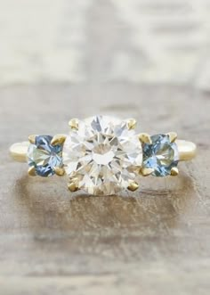 an engagement ring with three stones on the side and one stone in the middle, sitting on top of a wooden surface