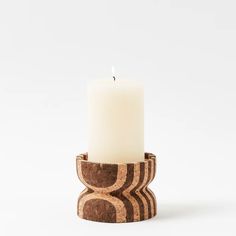 a white candle is sitting in a wooden holder on a white surface with an abstract design