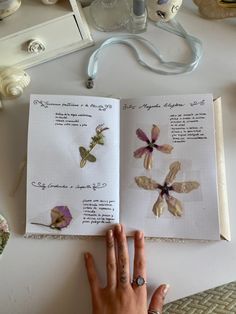 a person's hand is holding an open book with pressed flowers on the pages