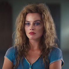 a woman with long hair and blue eyes looks at the camera while standing in front of a mirror