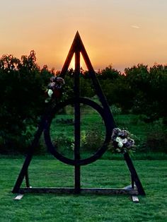 the sun is setting in the distance behind an iron sculpture with flowers on it's sides