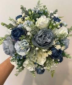 a bouquet of blue and white flowers is held up by someone's hand in front of a wall