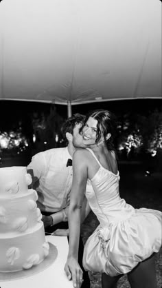 black and white photograph of a bride and groom leaning over a wedding cake on a table