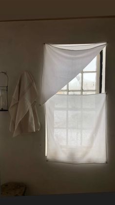 an open window with white curtains hanging from it's side and a towel hanging on the wall