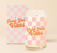 a candle with the words trust you vibes on it next to a pink and white checkered box