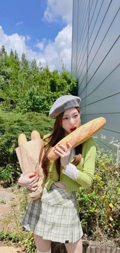 a girl in a green shirt and plaid skirt holding bread on her shoulder while standing next to a building