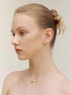 a woman wearing a gold necklace and earring with two small yellow flowers on it