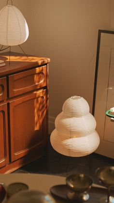 a white lamp sitting on top of a wooden dresser next to a mirror and bowl