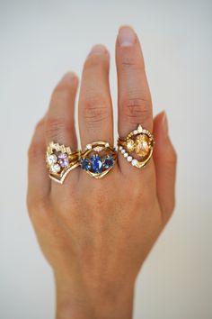 a woman's hand holding three rings with different colored stones on them and gold