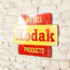 a red and yellow kodak sign on a white brick wall with words we sell kodak products