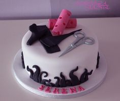 a white cake with black icing and pink fondant decorations on it, including scissors