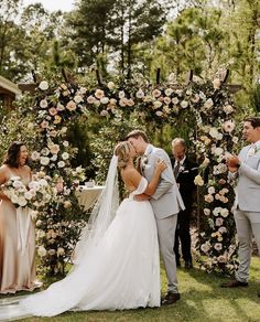 a bride and groom kissing in front of an outdoor ceremony arch with flowers on it