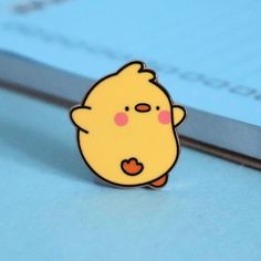 a pin with a small yellow chick on it's lap sitting next to a book