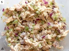 a bowl filled with chicken salad on top of a wooden table next to a measuring cup