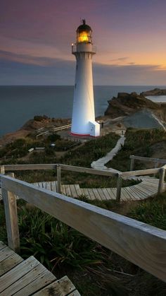 a light house sitting on top of a wooden ramp next to the ocean at sunset