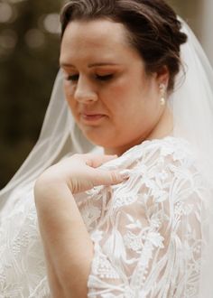 a woman in a wedding dress looking down at her hand on her shoulder and wearing a veil