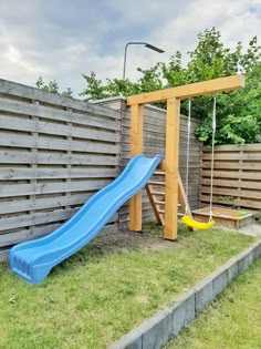 a wooden swing set with a blue slide in the back yard next to a fence