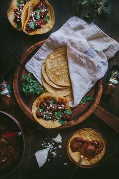 tortillas with meat and salsa on a wooden platter next to condiments