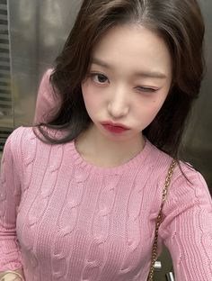 a young woman holding a cell phone in her right hand and wearing a pink sweater